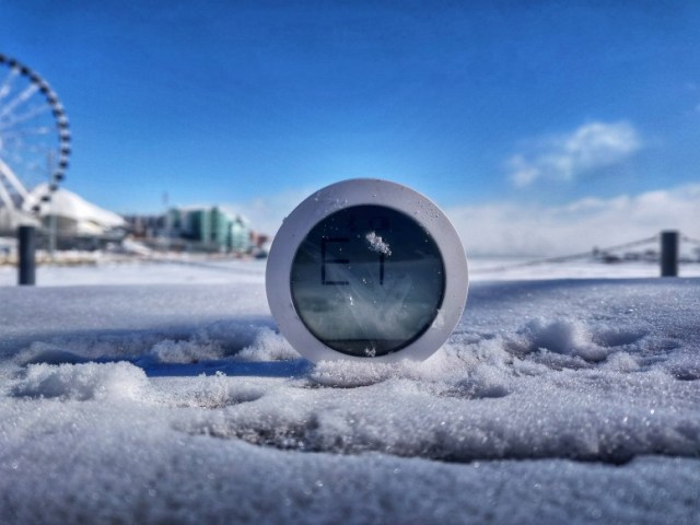 Round Xiaomi Bluetooth thermometer showing an E1 error, half-buried in snow with Chicago's Navy Pier Ferris wheel visible in the background