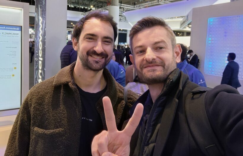 The author and Akis posing together at a Qualcomm booth, likely at MWC, Mike flashing a peace sign