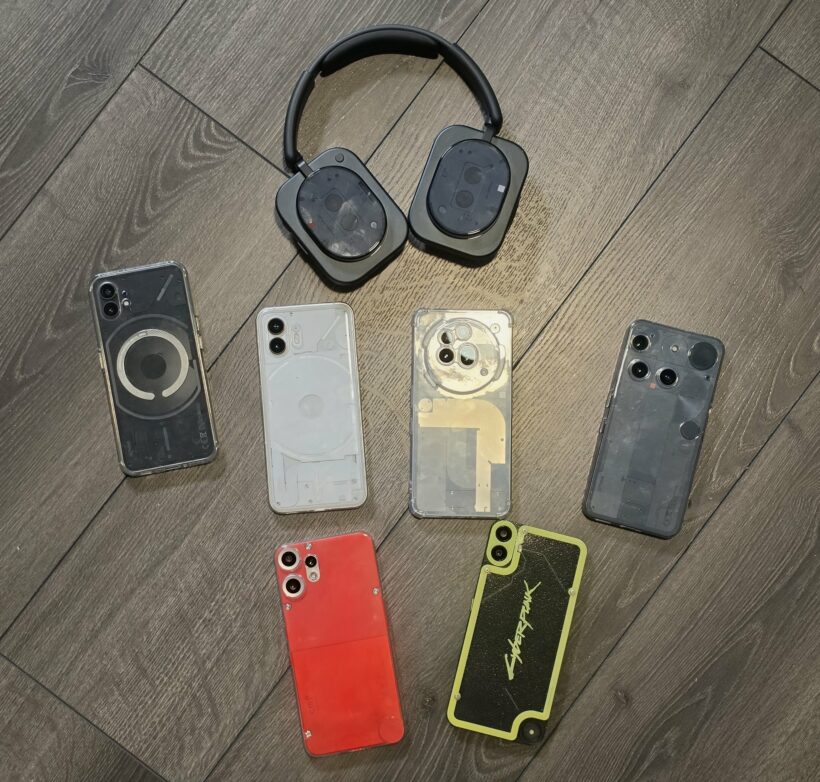 A collection of Nothing phones across multiple generations alongside Nothing headphones, including a Cyberpunk edition, laid out on a wood floor