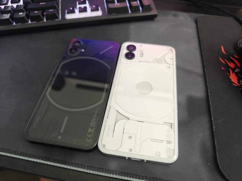 Two Nothing phones side by side on a desk, black and white versions, showing the transparent back design with visible internal components and Glyph elements