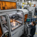Technician operating a metal additive manufacturing machine producing a complex part in a factory setting