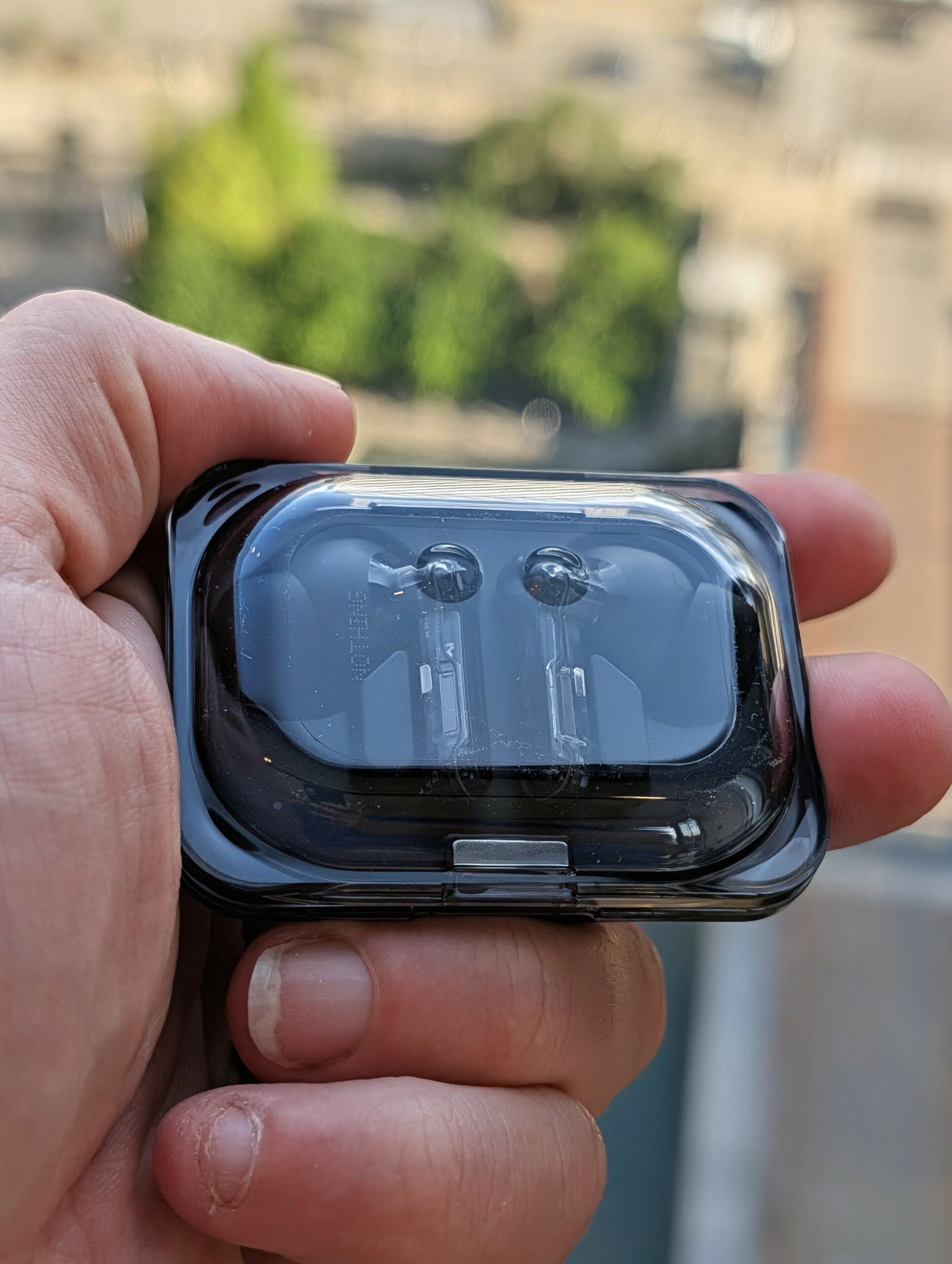 Hand holding a black transparent protective case containing wireless earbuds