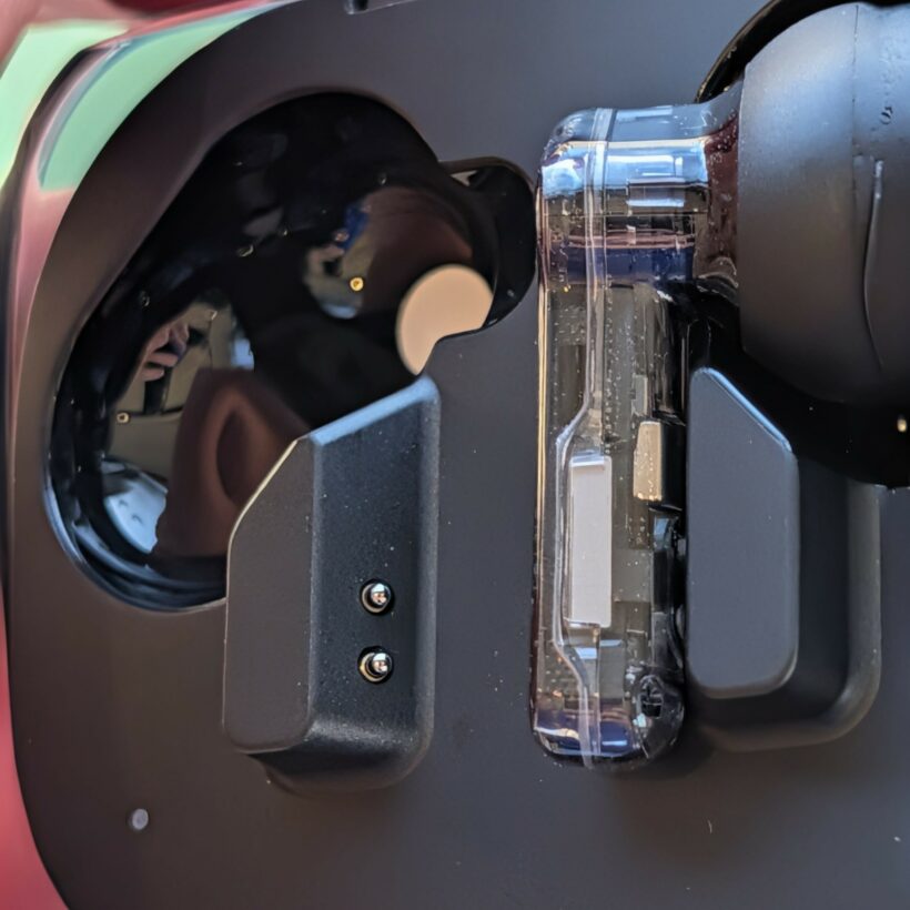 Close-up of a Tesla charging port with a transparent EV charging connector partially inserted, showing internal components and charging contacts