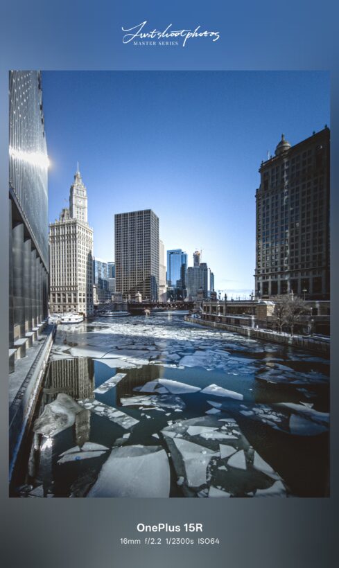 OnePlus 15R ultrawide sample shot at 16mm f/2.2: ice-covered Chicago River flanked by downtown skyscrapers under a clear blue sky
