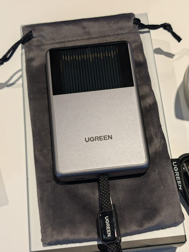 UGREEN MagFlow Pro power bank with front window showing internal cooling fins, resting on its pouch with built-in cable visible