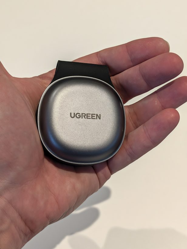 UGREEN MagFlow foldable 2-in-1 charger held in a palm, showing its small round metal magnetic charging puck folded shut