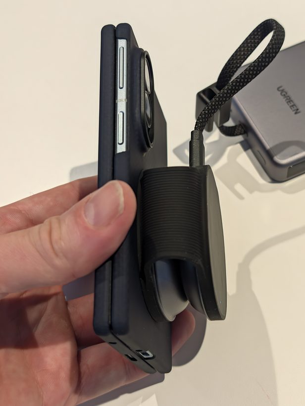 Hand holding a phone in a case beside a small UGREEN foldable magnetic charger with its USB-C cable, next to the MagFlow Pro power bank